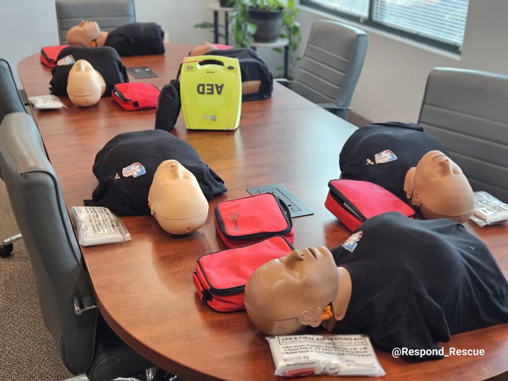 CPR manikins, first aid kits and an AED trainer set up on a conference room table for an on-site workplace CPR class.