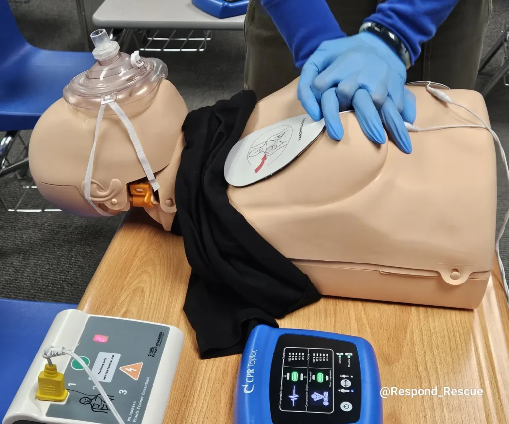 CPR and AED training on a manikin in a school classroom with an AED trainer and CPR feedback monitor